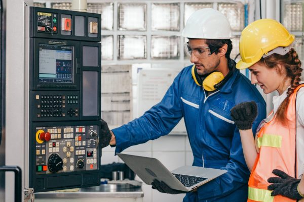 Male industrial engineer worker in hard helmet with female assistant using laptop control machine. Man and woman technician people working in heavy industry manufacturing factory.