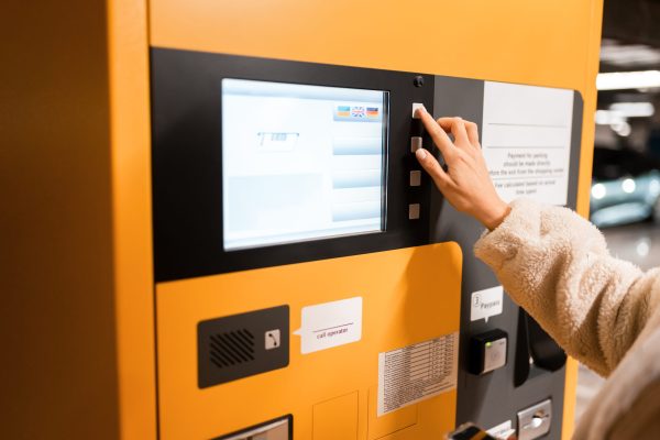Female hand presses button on a parking payment terminal. Elegant young girl pays for ticket in parking meter. Woman near terminal in the underground parking